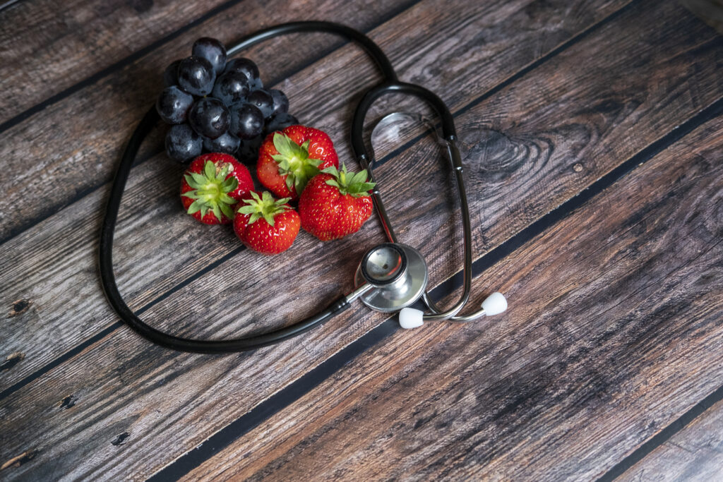 red scottish strawberries and black grapes with stethoscope on top of wooden table. medical and healthy food conceptual.