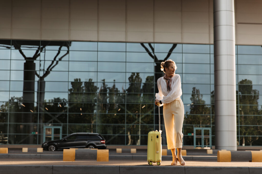 charming blonde woman in white blouse, beige pants and eyeglasses moves near airport. pretty girl i